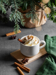 White mug with hot chocolate with whipped cream, cinnamon and anise on a wooden board