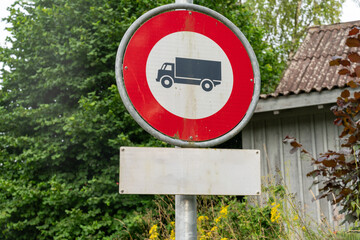 "No truck entry" sign . Old building surrounded by trees in the background.
