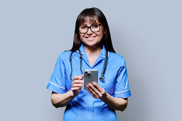 Portrait of smiling female nurse with smartphone, on grey studio background