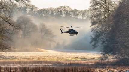Fototapeta premium Helicopter flying low over frosty field and woodland in morning mist.