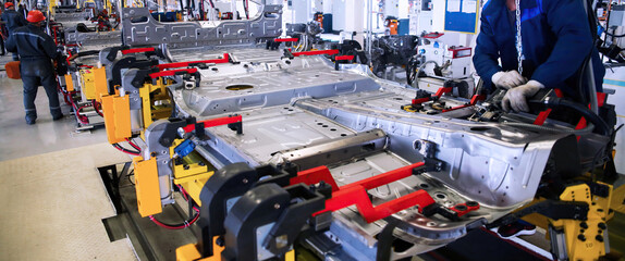 Workers assembling a vehicle chassis in a modern manufacturing facility during daylight hours.