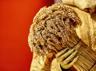 Golden wheat bouquet held by a statue against a vibrant red background during a festive celebration, showcasing exquisite craftsmanship and artistry