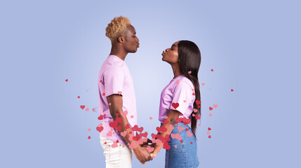 A loving black couple stands in front of purple backdrop, holding hands and sharing a sweet kiss. They celebrate their bond with heart-shaped decorations, symbolizing affection and togetherness.