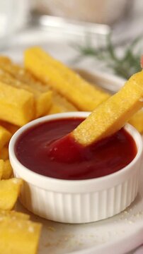 Dipping roasted polenta fries in tomato sauce. Vertical video. Close-up.