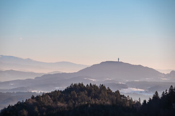 Obraz premium Panoramic view of Pyramidenkogel in Rosental Valley in winter seen from mount Petelin in Faak, Carinthia, Austria. Alpine landscape in soft light. Austrian Alps shrouded in mist. Serenity and calmness