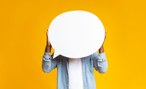 Unrecognizable black guy holding empty speech bubble in front of his head over yellow studio background, copy space