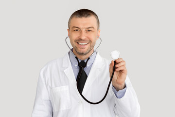 Medical Checkup Concept. Portrait of smiling confident mature general practitioner holding stethoscope, ready to examine patient, standing isolated over white studio background, looking at camera