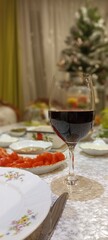 a large glass goblet on a thin stem, half filled with red wine, stands on a New Year's table with a decorated New Year's tree on a blurred background