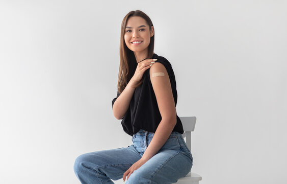 Pretty young woman getting vaccinated against covid-19, showing arm with adhesive bandage on light studio background. Female patient after receiving coronavirus vaccine shot. Population immunization