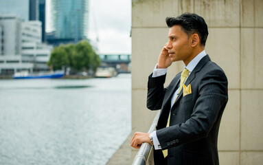 Serious, smartly dressed Asian / Middle eastern businessman holding a mobile phone to his ear, in an outdoor city location.