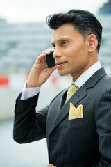 Serious, smartly dressed Asian / Middle eastern businessman holding a mobile phone to his ear, in an outdoor city location.
