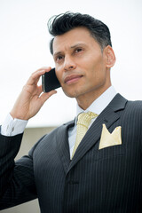 Serious, smartly dressed Asian / Middle eastern businessman holding a mobile phone to his ear, in an outdoor city location.
