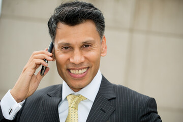Smiling smartly dressed Asian / Middle eastern businessman holding a mobile phone to his ear, in an outdoor city location.