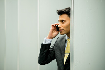 Serious, smartly dressed Asian / Middle eastern businessman holding a mobile phone to his ear, in an outdoor city location.