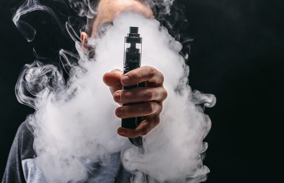 Unrecognizable man in the cloud of vape smoke. Guy smoking e-cigarette to quit tobacco. Vapor and alternative nicotine free smoking concept, copy space