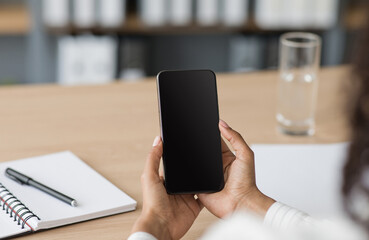 Business woman calls online in office, new normal and social distance. Millennial african american woman sitting at table and looking on smartphone with blank screen, close up, cropped, indoors