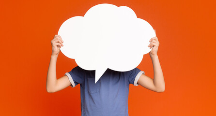 Little boy holding an empty speech bubble in front of his head, orange studio background, free space