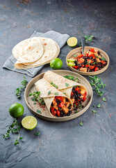 Mexican style burritos - tortilla wrap with spicy chicken meat breast filet nuggets, vegetables and black olives served as close-up with hot spices on a design plate