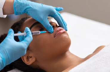 Black lady getting lip filling injection at modern beauty salon, closeup, copy space