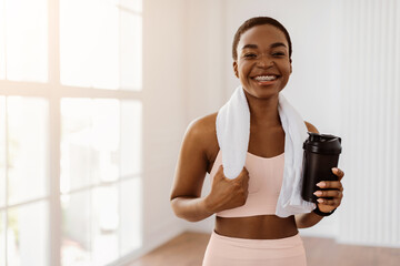 Portrait of sporty beautiful smiling sporty woman in white sportswear and towel on neck holding shaker with healthy drink, whey protein, fresh water or coffee isolated, posing looking at camera