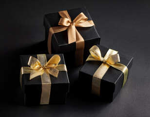 Obraz premium three black cardboard gift boxes with gold ribbon on black background