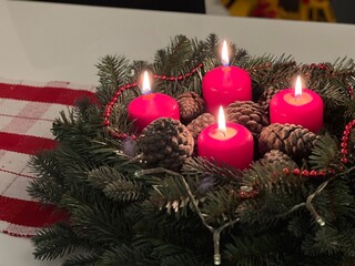Close up of an advent wreath with four red burning candles on white table 