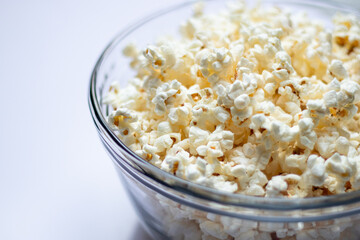 Close up of tasty popcorn in a glass bowl on white table background 