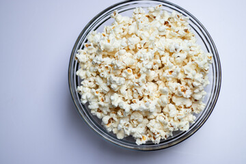 Top view of tasty popcorn in a glass bowl on white table background 