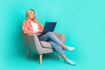 Full size photo of pretty mature female sit armchair netbook wear trendy plaid outfit isolated on aquamarine color background
