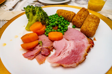 Roast dinner of consisting of roast gammon, peas, carrots, broccoli and croquet potatoes