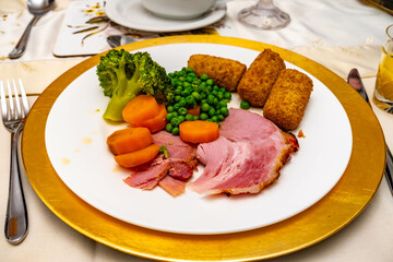 Roast dinner of consisting of roast gammon, peas, carrots, broccoli and croquet potatoes