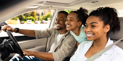 Happy Black Parents And Daughter Riding A Car Smiling Looking Aside Sitting In Seats Enjoying Road Trip By Auto. Automobile Tourism, Traffic And Transportation Concept. Side View, Selective Focus