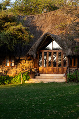 Luxury resort experience, at traditional African game lodge, welcome entrance with cement stairs, wood doors, and thatch roof in early morning sunlight, Lewa Conservancy, Kenya, Africa
