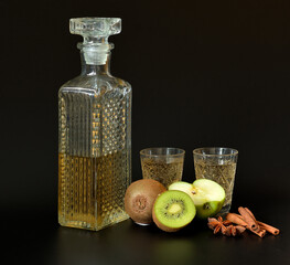 Apple-kiwi liqueur with cinnamon and anise in a crystal decanter and two glasses on a black...
