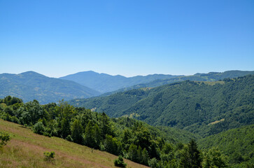 Fototapeta premium Serene mountain landscape showcasing rolling green hills under a clear blue sky, capturing the essence of nature's tranquility and beauty. Ideal for themes of outdoor adventure or peaceful retreats