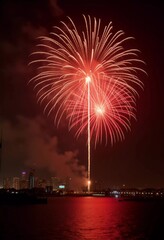 Brilliant red and gold fireworks explode against the dark sky, reflecting in the waterway. The celebration lights up the city skyline during a festive nighttime event. Generative AI