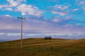 Tranquil rural landscape. Wooden utility pole and a weathered barn sit atop a grassy hill under a cloudy sky. Quiet countryside scene. , Newcastle, Wyoming, USA.