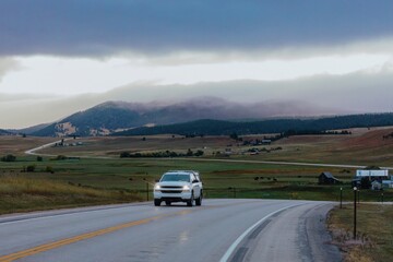A white pickup truck drives along a winding highway through a rural landscape. Misty mountains in...