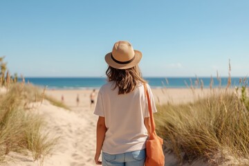 Obraz premium Woman enjoying a serene beach walk on a sunny day with soft waves and golden sands in the background