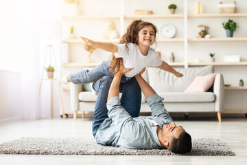 Adorable little curly girl spending time with her daddy at home, middle-eastern young man father...