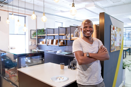 Attractive, charming young African American male entrepreneur in coworking space coffee shop counter smiling confidently