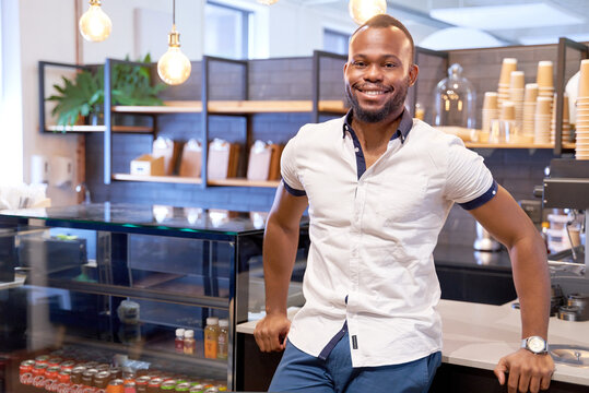 Attractive, charming young African American male entrepreneur in coworking space coffee shop counter smiling confidently