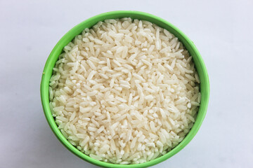 Raw rice is contained in a small green bowl, isolated on a white background