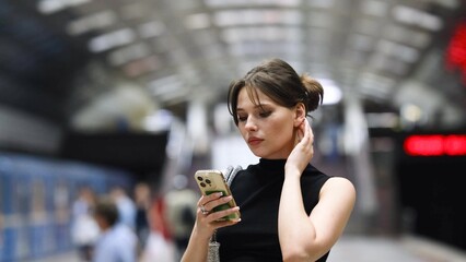 Stylish young woman reading a text message on her mobile phone while waiting for a subway train