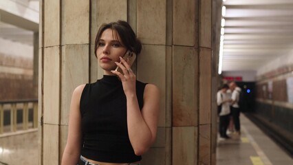 A beautiful brunette talks on the phone while waiting for her train at the metro station.
