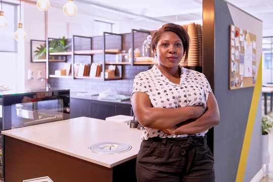 Portrait of natural smiling black professional businesswoman with arms crossed in modern coffee shop
