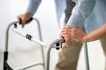 Unrecognizable elderly man using walker, young doctor supporting and helping him at retirement...