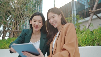 Asian Businesswomen Collaborating Outdoors: Sharing Ideas and Plans with a Tablet in an Urban Greenery Setting. Professional Asian Women Discussing Digital Marketing. Remote work online outdoors