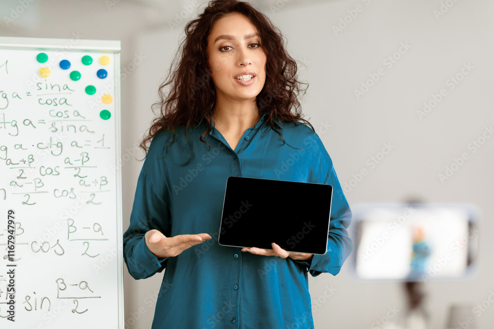 Aufkleber Modern Distance Learning. Lady math teacher making video conference chat with students using cellphone on tripod, holding and showing tablet with empty screen with copy space for mock up, explaining