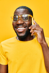 Smiling young man wearing glasses and a yellow t shirt, talking on the phone against a bright yellow background, conveying joy and positivity with vibrant colors